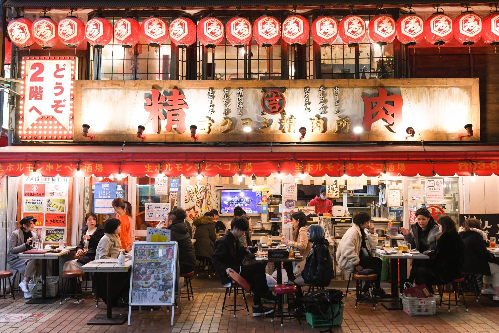 Tokyo izakaya exterior with red lanterns, signs, and diners