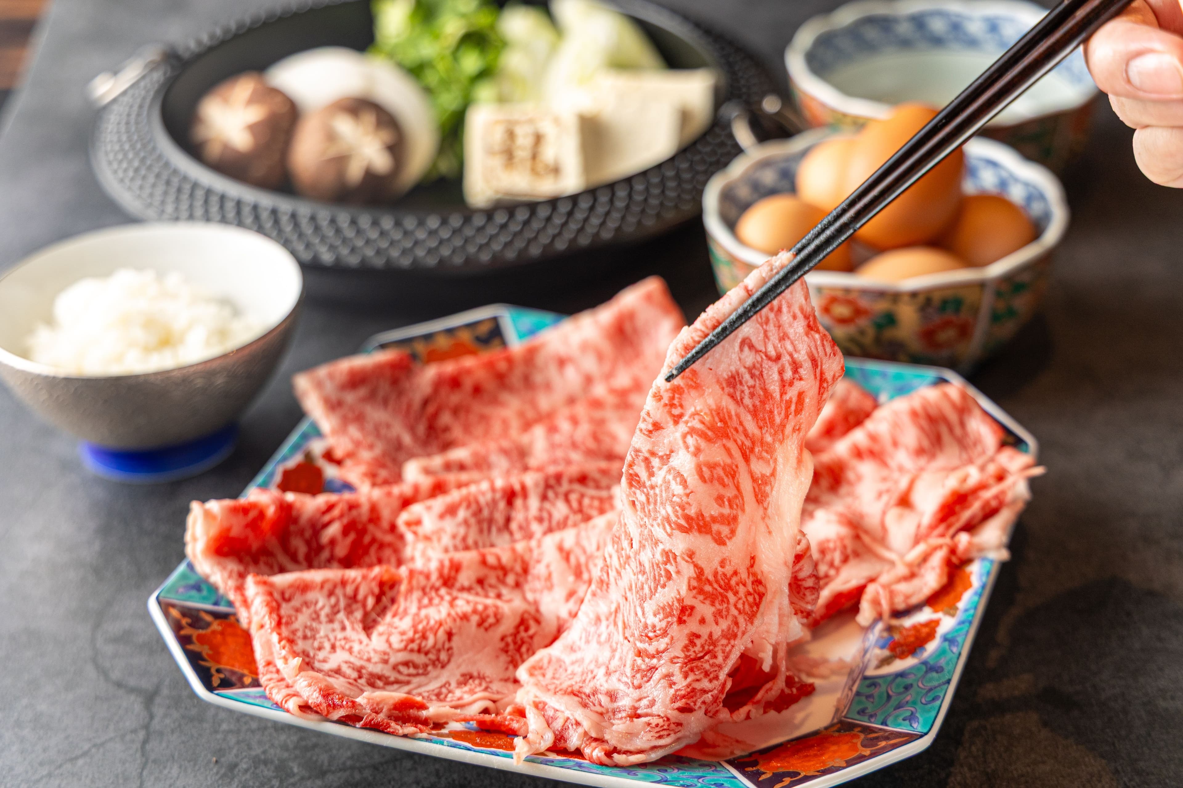 Thin slices of wagyu beef being lifted with chopsticks at a Japanese meal
