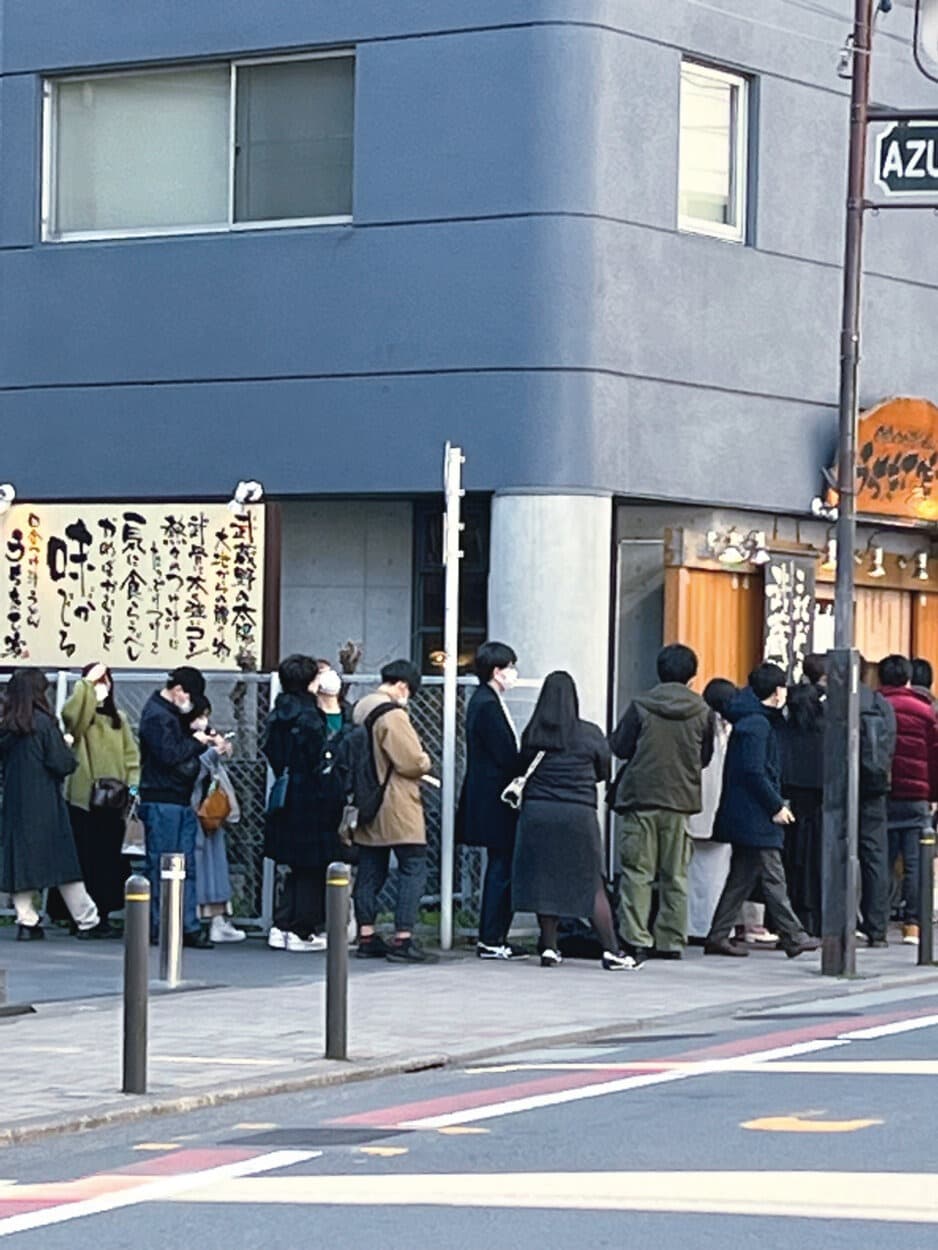 People lining up on a sidewalk outside a Tokyo restaurant