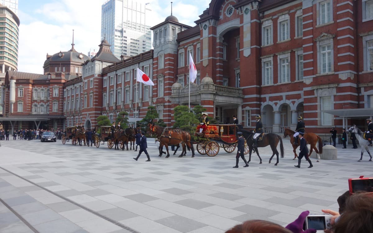 Travelers and a formal procession outside a large city station