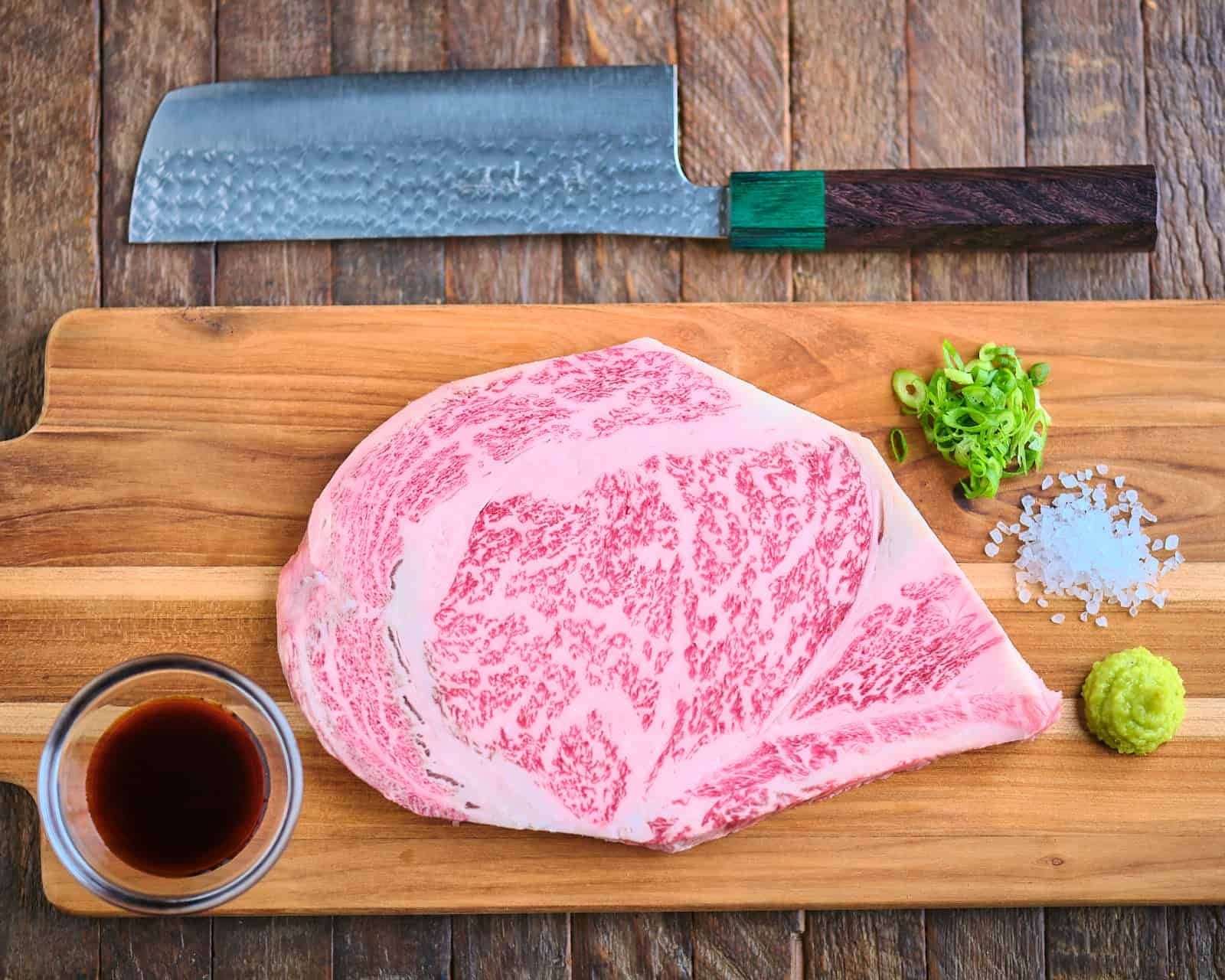 Raw wagyu beef cut on a wooden board with a Japanese knife and condiments