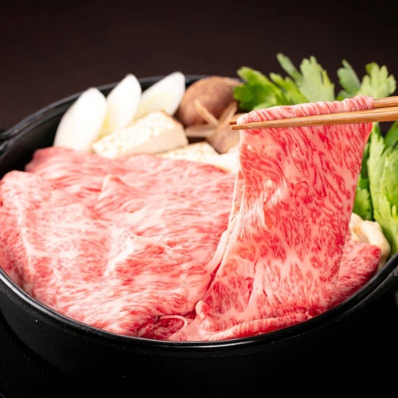 Thinly sliced wagyu beef being lifted above a hot pot